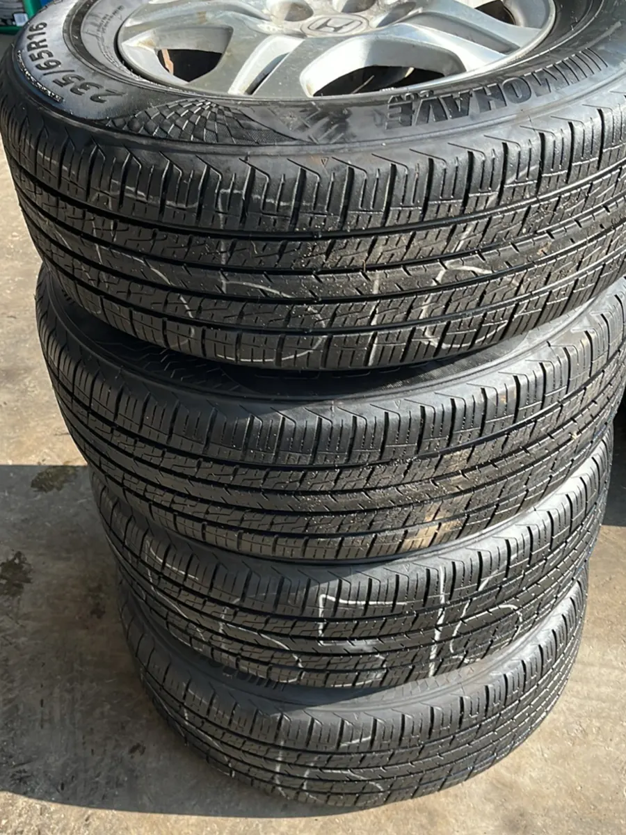 Four passenger tires mounted on wheels and stacked outside the shop